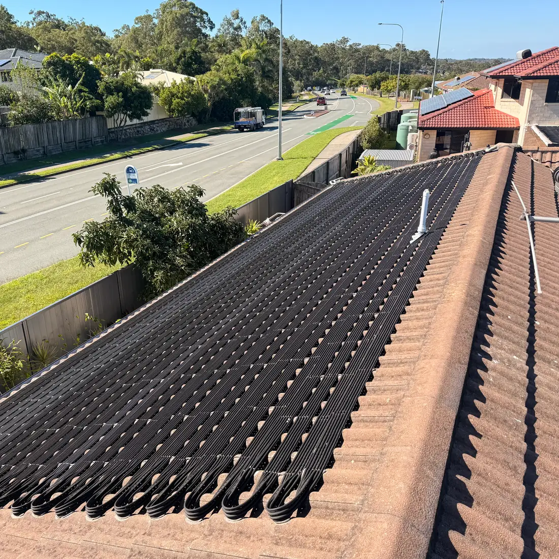 Rooftop solar pool heating strip matting running down a tile roof, with looped header pipework along the bottom edge